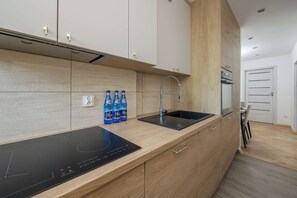 Eine moderne Küche mit Holzschränken, einer schwarzen Induktionskochplatte, einer Edelstahl-Spüle und einem eingebauten Backofen.