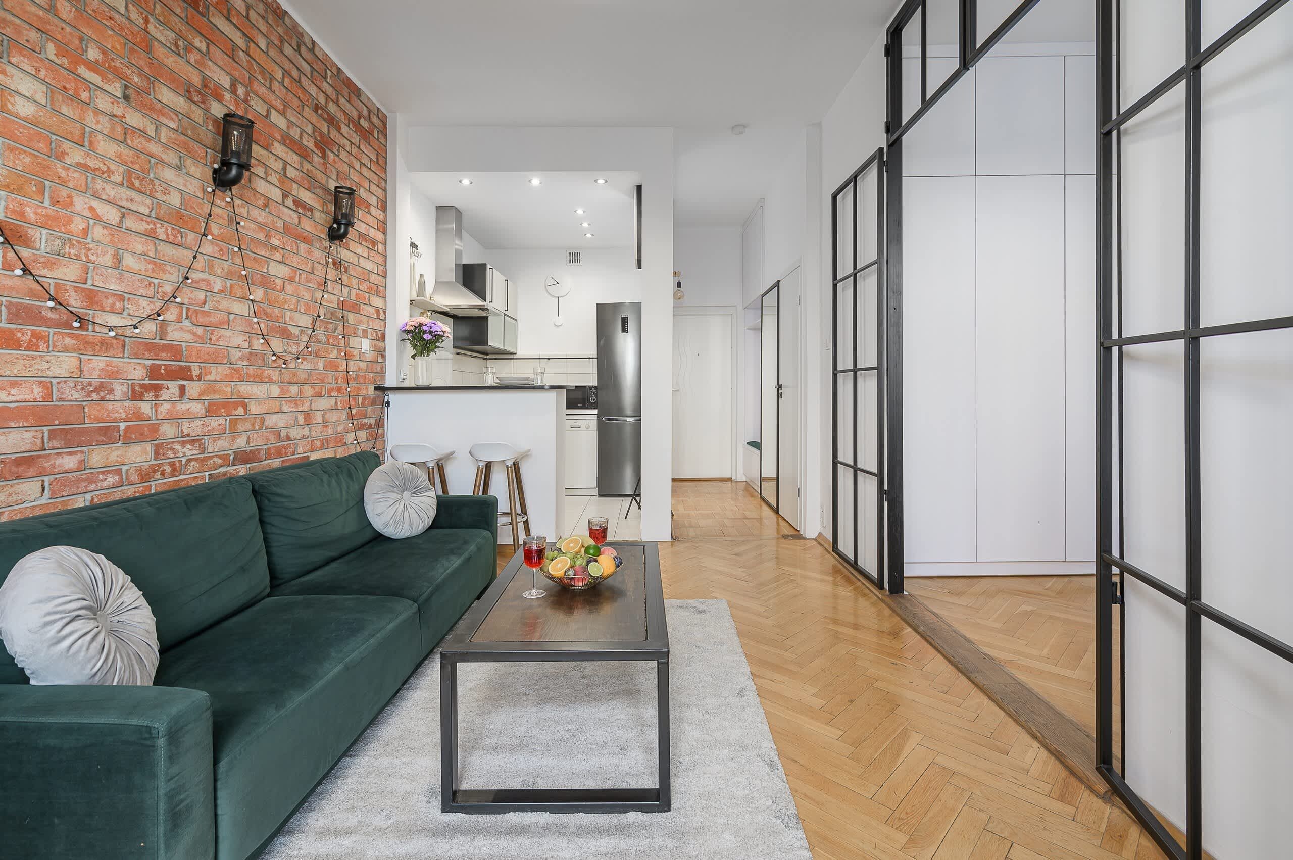 A modern living room with a green sofa, a coffee table with fruit, and a brick wall.