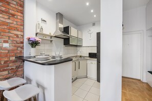 Cozinha moderna com armários brancos, bancada preta e parede de tijolos.