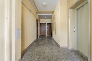 A narrow hallway with a textured wall, a door at the end, and a metal locker on the right. - Lumina 2-room Apart w/ Balcony Center & City View (Warszawa)