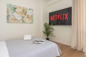 A hotel room with a bed, a painting, a potted plant, and a TV displaying the Netflix logo. - Lumina 2-room Apart w/ Balcony Center & City View (Warszawa)