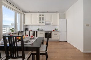 Eine moderne Küche mit weißen Schränken, einem Esstisch für zwei Personen und Blick auf die Stadt durch ein großes Fenster.