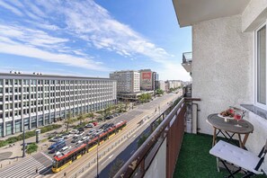 Ein Balkon mit Blick auf eine Stadtstraße, eine Straßenbahn und ein Gebäude mit einer großen Werbetafel.