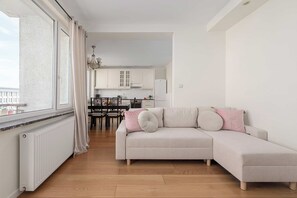 A modern living room with a sofa, a dining area with a table and chairs, and a kitchen with cabinets and appliances. - Lumina 2-room Apart w/ Balcony Center & City View (Warszawa)