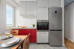 A modern kitchen with a built-in oven, a stainless steel refrigerator, and a window providing a view of the cityscape. - Lumina 3-room Apart w/ Balkony in the Center (Warszawa)