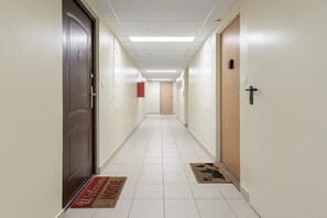 A hotel corridor with a red welcome mat, a wooden door, and a light switch on the wall. - Lumina 3-room Apart w/ Balkony in the Center (Warszawa)