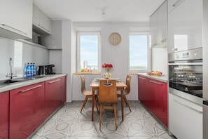 A modern kitchen with a dining table, chairs, a clock, and a view through the windows. - Lumina 3-room Apart w/ Balkony in the Center (Warszawa)