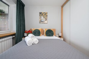A neatly made bed with rolled towels, a painting on the wall, and a window with curtains. - Lumina 3-room Apart w/ Balkony in the Center (Warszawa)