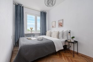 Une chambre à coucher comprenant un lit, une table de chevet, une fenêtre avec des rideaux et deux tableaux accrochés au mur.