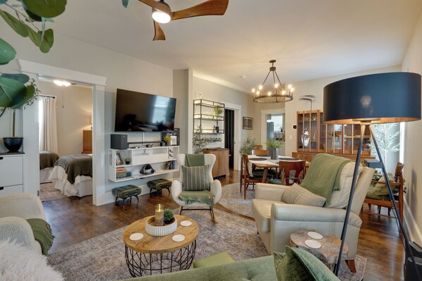 A spacious living room with a flat-screen TV, a dining area, and a kitchen in the background. - 'Olive & Oak' Mid-Century Sedalia Home w/ Patio (Sedalia)