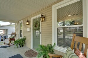 A covered porch with a door, two wall-mounted lanterns, a bench, and potted plants. - 'Olive & Oak' Mid-Century Sedalia Home w/ Patio (Sedalia)