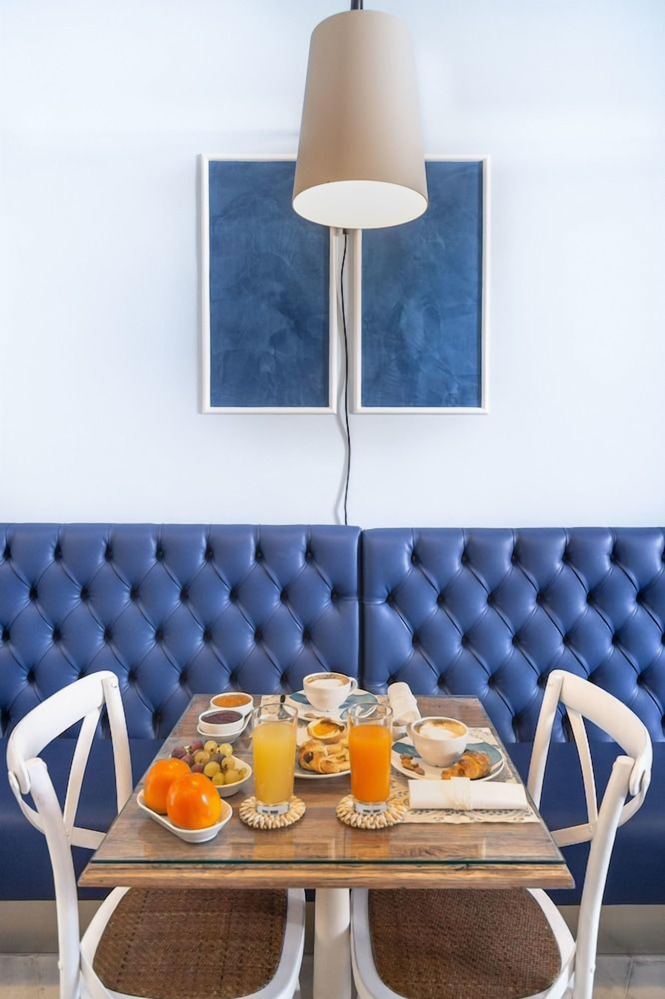 A dining area with a blue upholstered booth, a glass table with breakfast items, and a pendant light.