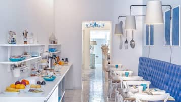 Una cocina moderna con armarios blancos, una isla central con cestos de fruta y un banco tapizado en azul.
