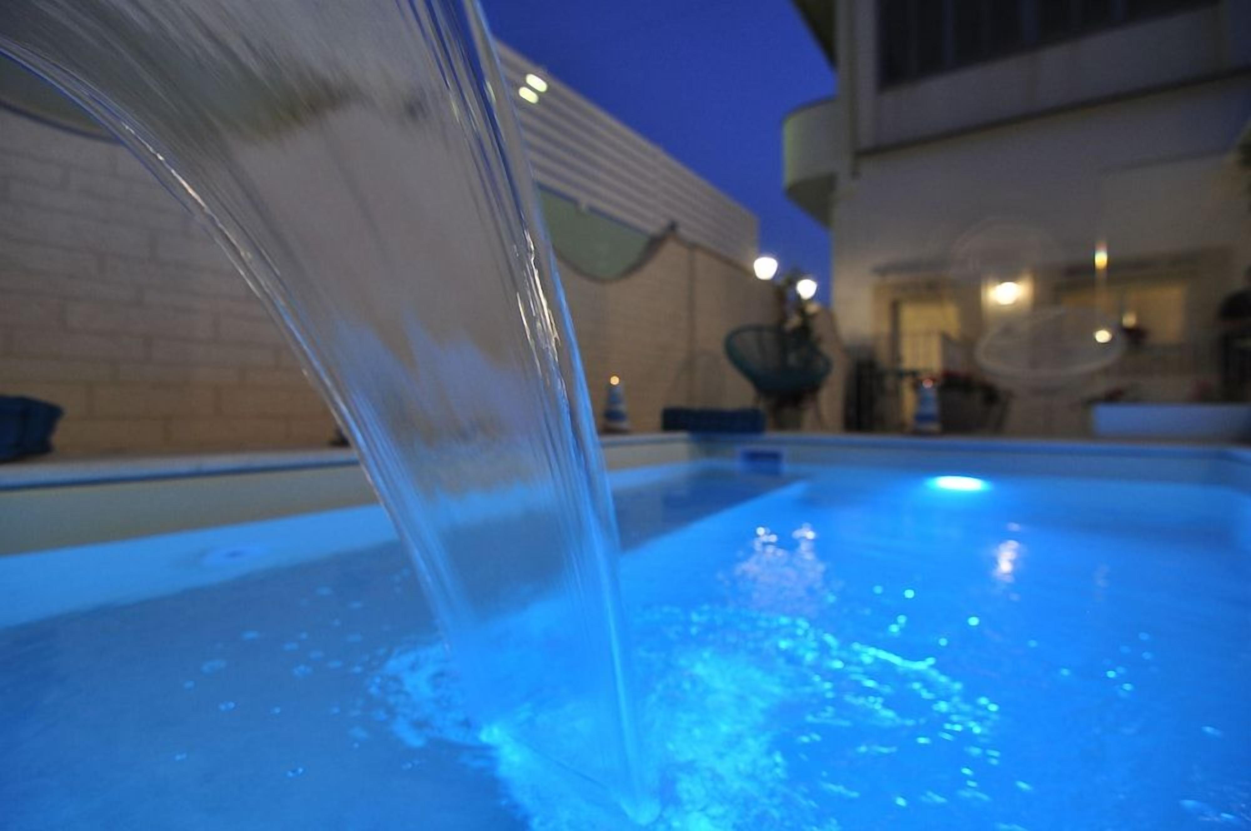 A pool with water cascading over the edge, surrounded by a building with a brick wall and outdoor seating.