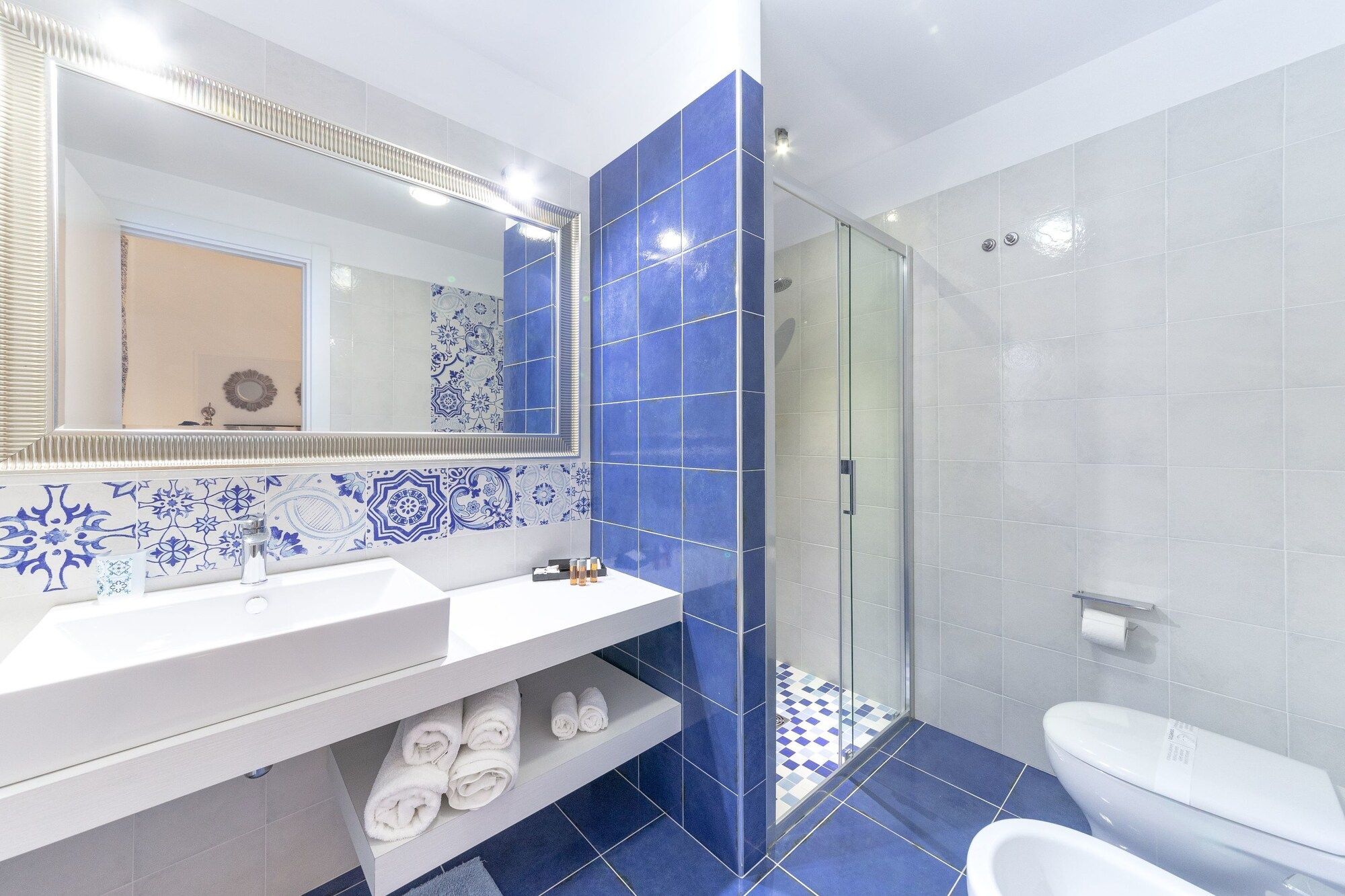 Un baño moderno con tocador blanco, un espejo grande y azulejos azules.