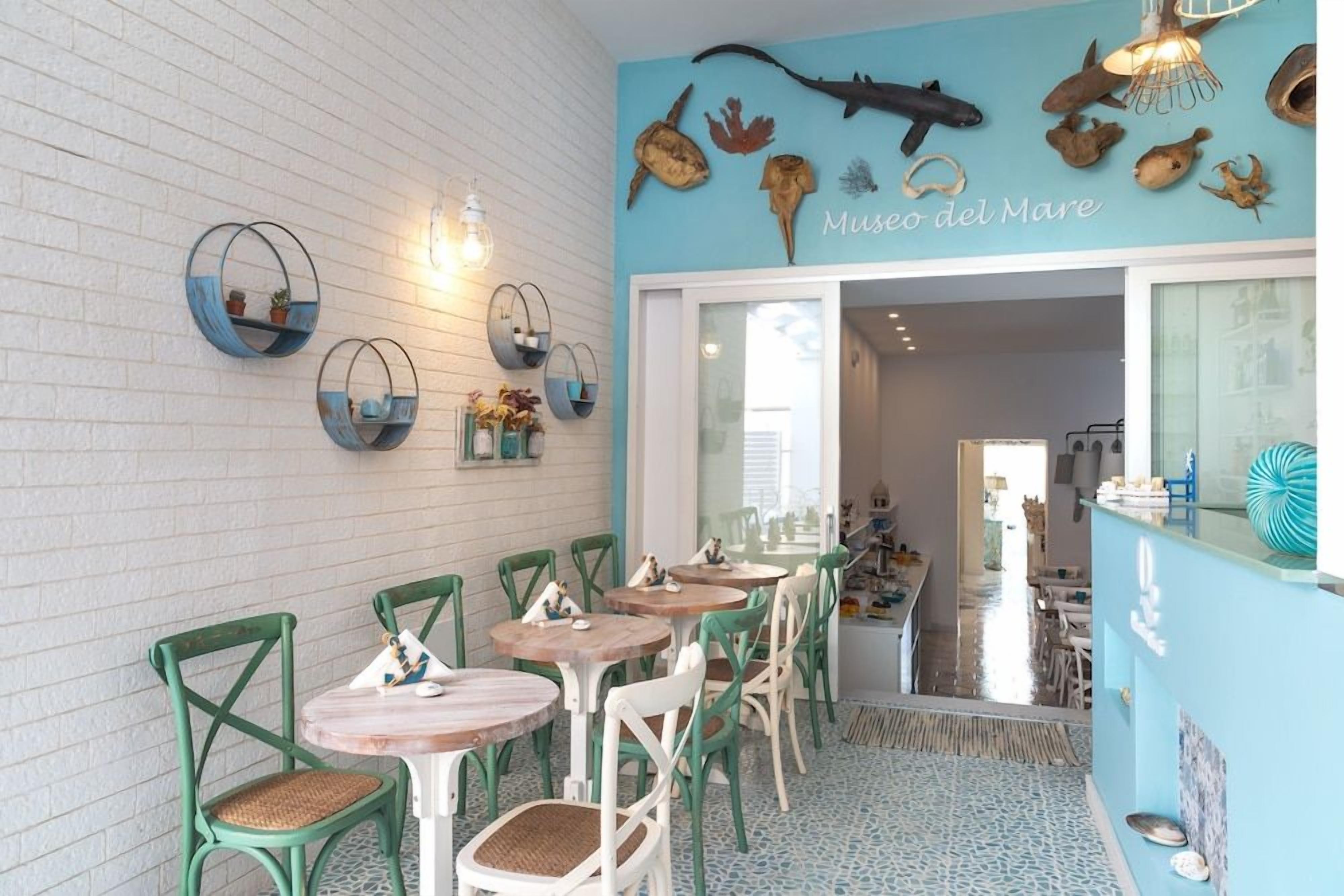 A restaurant interior with round tables and chairs, a wall with marine-themed decorations, and a visible entrance to another area.