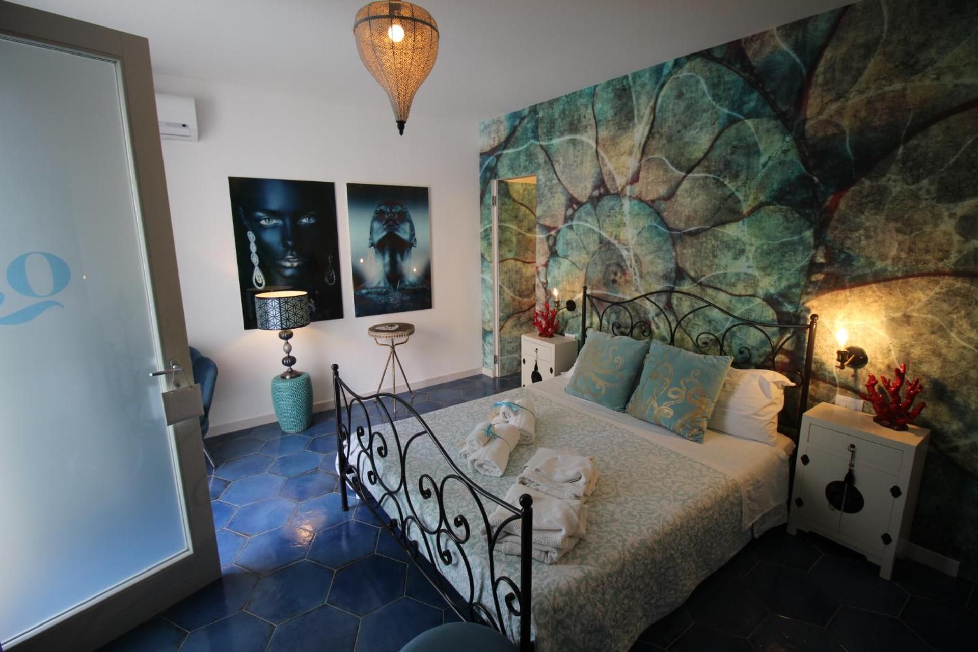 Un dormitorio con cama, mesita de noche, lámpara y una pared decorada con arte abstracto.