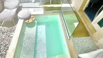 A rooftop pool area with a glass balustrade, lounge chairs, and a seating area with patterned cushions.
