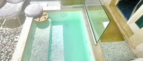 A rooftop pool area with a glass balustrade, lounge chairs, and a seating area with patterned cushions.