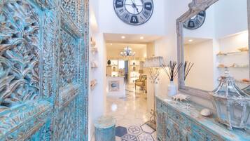 A hallway with a decorative blue door, a large wall clock, and a mirror reflecting a chandelier.