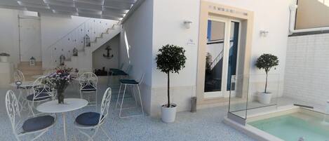 Un espacio al aire libre techado con mesas y sillas, una piscina pequeña y una escalera que lleva a un nivel superior.