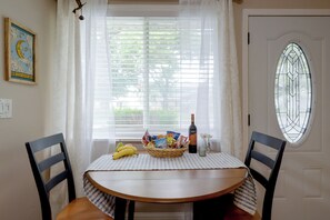 En matplats med ett bord dukat för två personer, en korg med snacks, en flaska vin och en vas med blommor.
