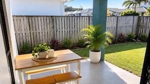 Una terrazza esterna con tavolo e panche in legno, una pianta in vaso e vista su un cortile recintato.