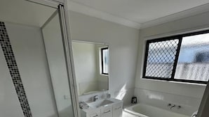 Un bagno moderno con cabina doccia in vetro, una vasca e una finestra che lascia entrare la luce naturale.
