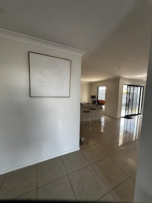 A spacious room with a large window, a framed artwork on the wall, and a kitchen area in the background.