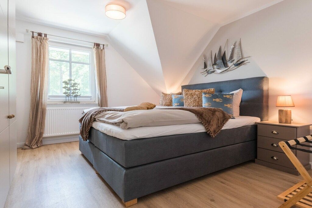 Quarto com cama, mesa de cabeceira, abajur, janela com cortinas e decoração na parede.