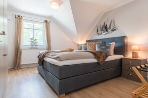 Une chambre à coucher comprenant un lit, une table de chevet, une lampe, une fenêtre avec des rideaux et un élément de décoration fixé au mur.