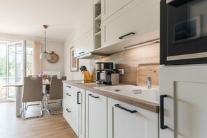 A modern kitchen with white cabinetry, a wooden countertop, a coffee maker, and a microwave. - Holiday apartment with 1 bedroom (Prerow)