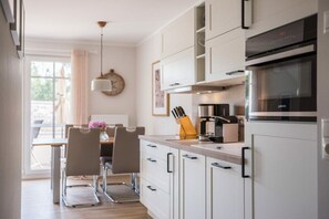 Eine moderne Küche mit weißen Schränken, einem Einbauofen und einem Essbereich mit Tisch und Stühlen.