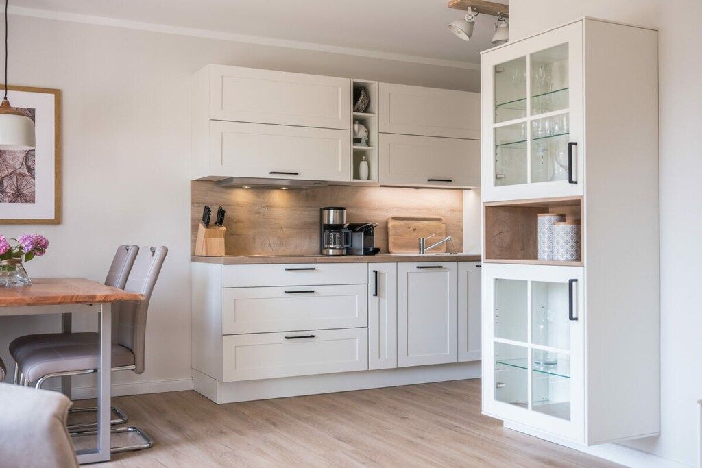 A modern kitchen with white cabinetry, a wooden countertop, and a dining area with a table and chairs.