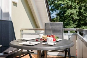 Ein runder Tisch mit einem weißen Teller, einer weißen Tasse und einer Obstschale auf einem Balkon.