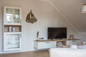Ein modernes Schlafzimmer mit Schrägdecke, einem Fernseher, einem Schrank mit Glastüren und einem dekorativen Wandbild eines Segelbootes.