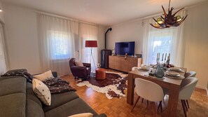 Ein Wohnzimmer mit Sofa, einem Esstisch für vier Personen, einem Fernseher und einem Kamin.