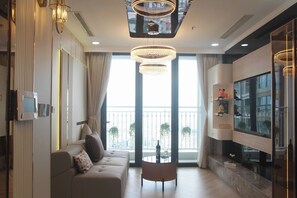 Una sala moderna con un sofá, una mesa de centro y un televisor. Amplias ventanas ofrecen vistas de la ciudad.