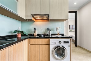 A modern kitchen with wooden cabinets, a built-in washing machine, and a countertop with various kitchen items. - Saira by Kozystay - Menteng (Central Jakarta)