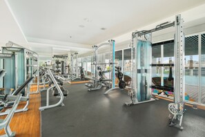 A modern gym with various exercise machines, large windows, and a view of the outdoors. - Saira by Kozystay - Menteng (Central Jakarta)