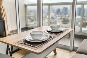 A dining table with two bowls and plates, set with cutlery, in a room with a city view through large windows. - Saira by Kozystay - Menteng (Central Jakarta)