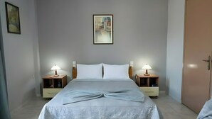 Un dormitorio con cama, dos mesitas de noche con lámparas, un cuadro enmarcado en la pared y una puerta.