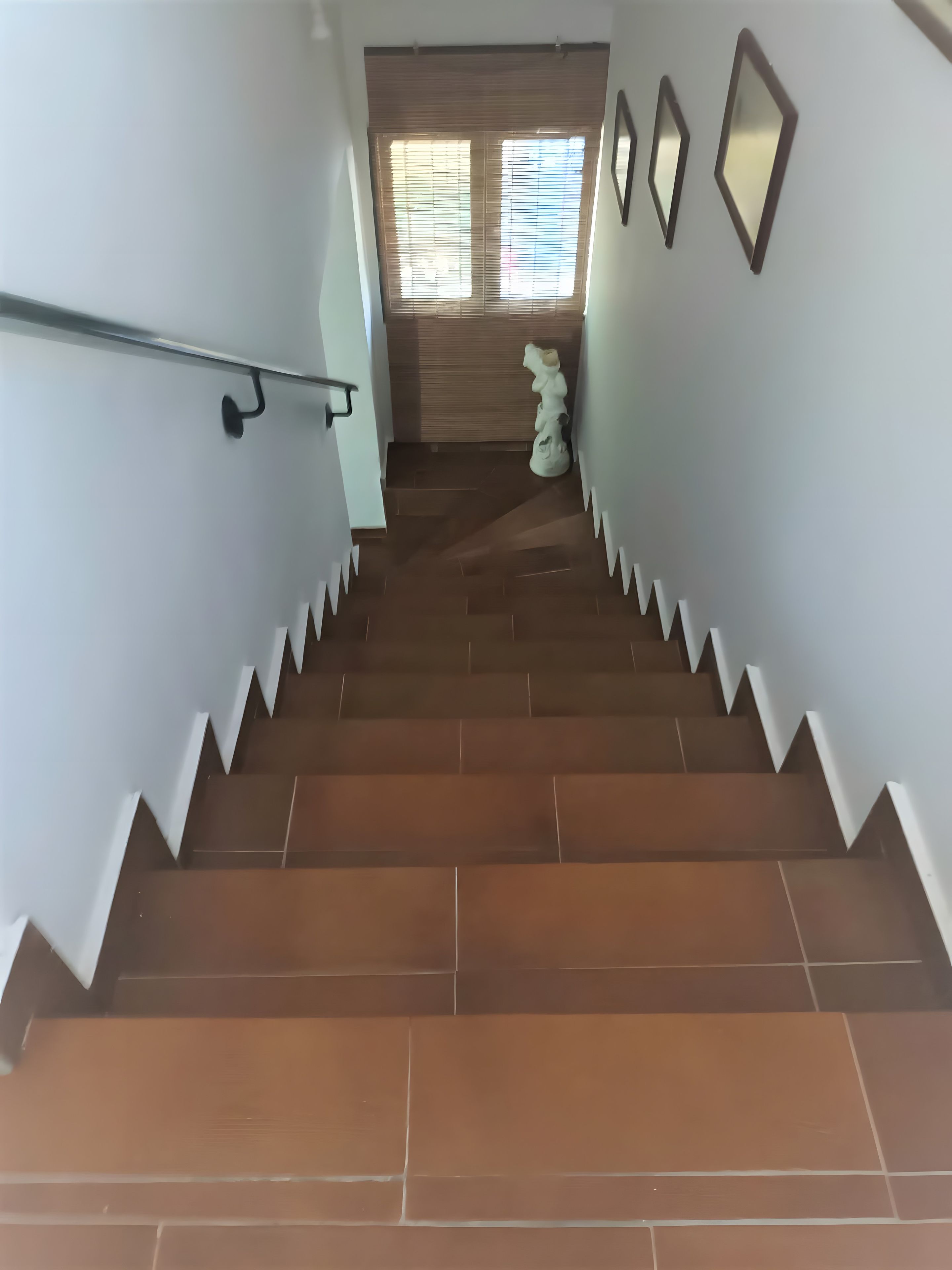 A staircase with a handrail, leading to a room with a window and a statue.