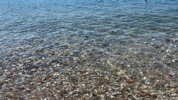Ein klarer See mit sichtbaren Kieselsteinen und Booten, umgeben von Bergen.