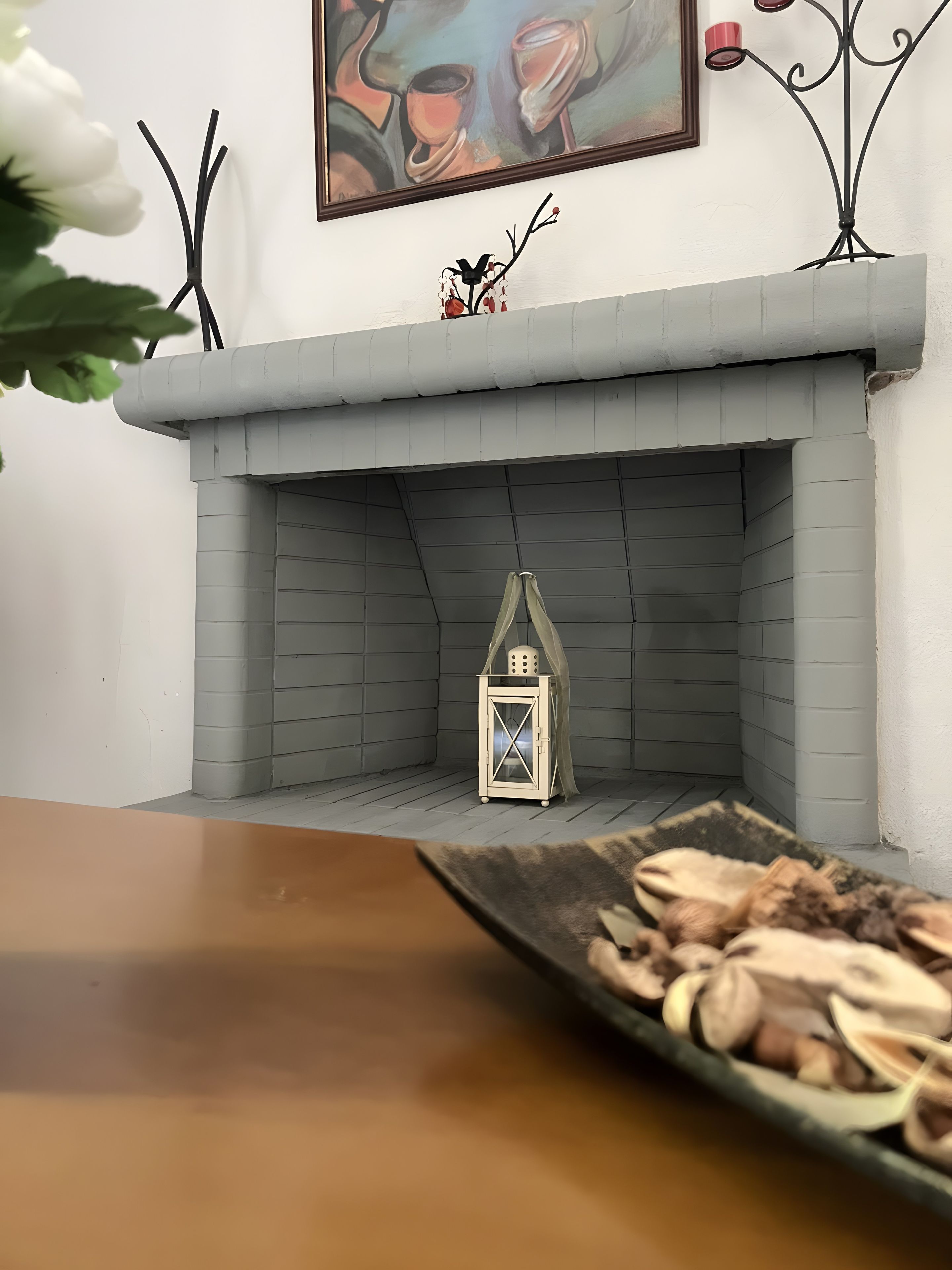 A fireplace with a decorative lantern, a framed painting above it, and a tray of nuts on a table in front.