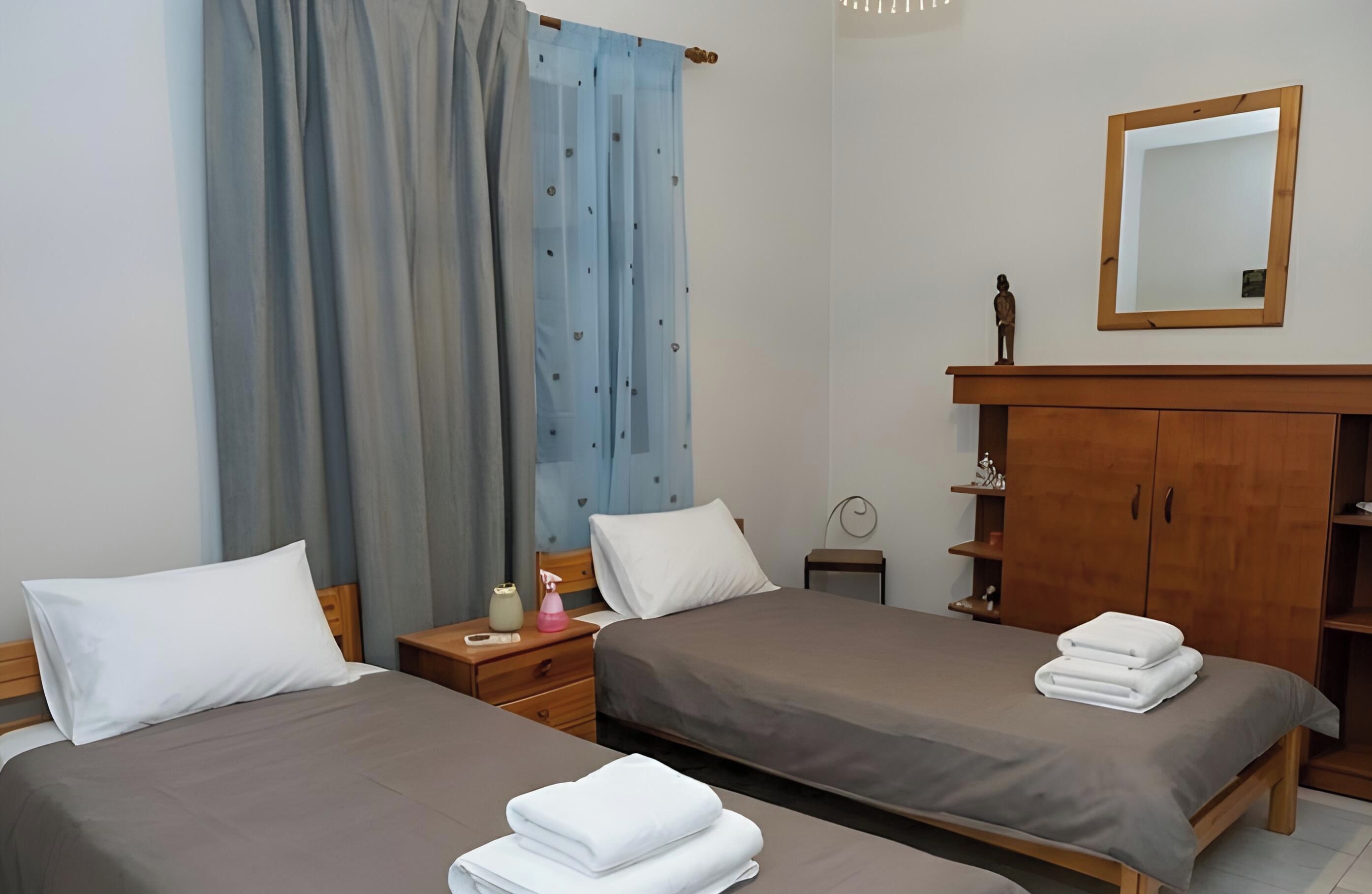 Une chambre d’hôtel avec deux lits, une armoire en bois, un miroir et une table de chevet avec une lampe.