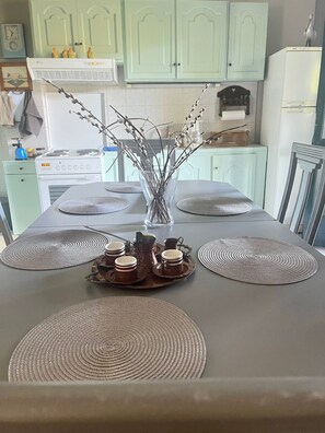 Une table à manger avec des sets de table, un vase décoré de branches et un plateau contenant des tasses et une carafe.