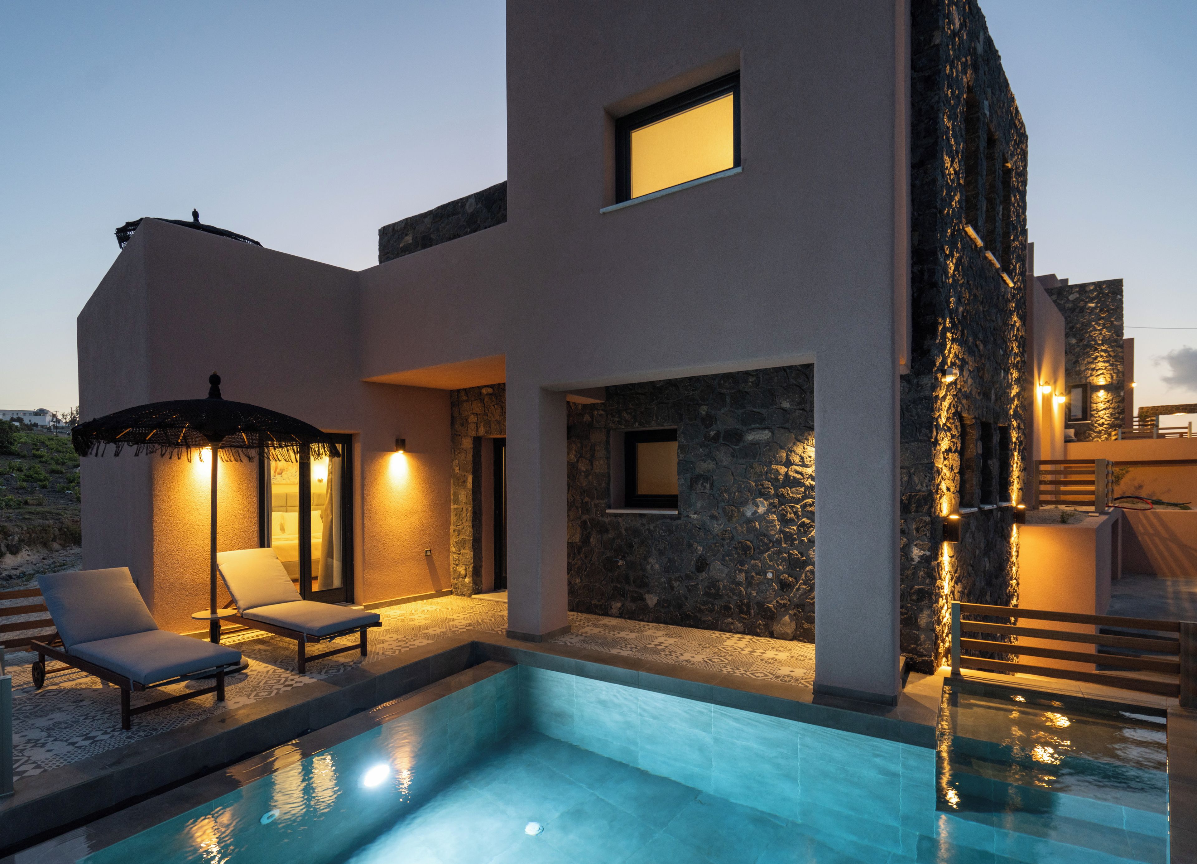 Un edificio moderno con piscina, sillones de descanso y una pared de piedra.