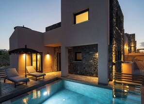A modern building with a swimming pool, lounge chairs, and a stone wall.