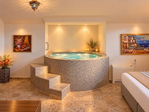 A spa room with a hot tub, a painting, and a potted plant.